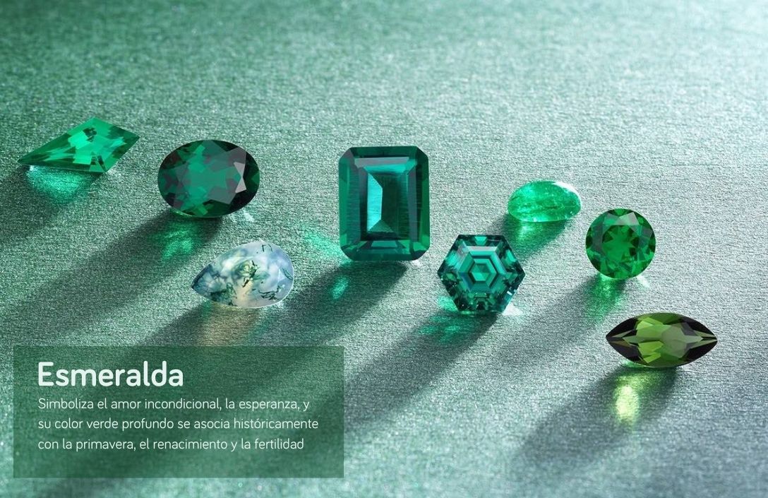 Colección de esmeraldas talladas sobre una superficie verde texturizada, ilustrando la guía de piedras de nacimiento de Joyería Marga Mira. La imagen presenta varias gemas esmeraldas verdes de diferentes formas: una lágrima, un óvalo grande, un rectángulo esmeralda central, un hexágono con patrón geométrico, un cabujón pequeño, un redondo brillante, una talla marquesa y otra forma geométrica alargada. En la esquina inferior izquierda, un recuadro con el título "Esmeralda" y el texto explicativo: "Simboliza el amor incondicional, la esperanza, y su color verde profundo se asocia históricamente con la primavera, el renacimiento y la fertilidad"